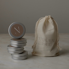 Candle tins with decorative lids on a marble surface, featuring a 'Natural Isle' drawstring bag.