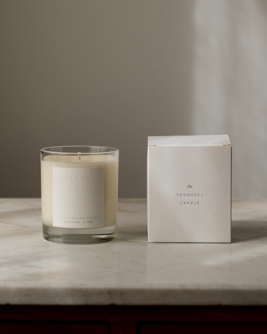 Natural Isle Yoonseul Candle and its packaging on a marble surface with a neutral background