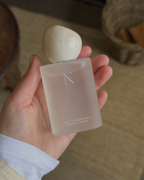 Natural Isle Signature Room Spray, Hand holding a white bottle labeled 'The Signature Room Spray' with a blurred background