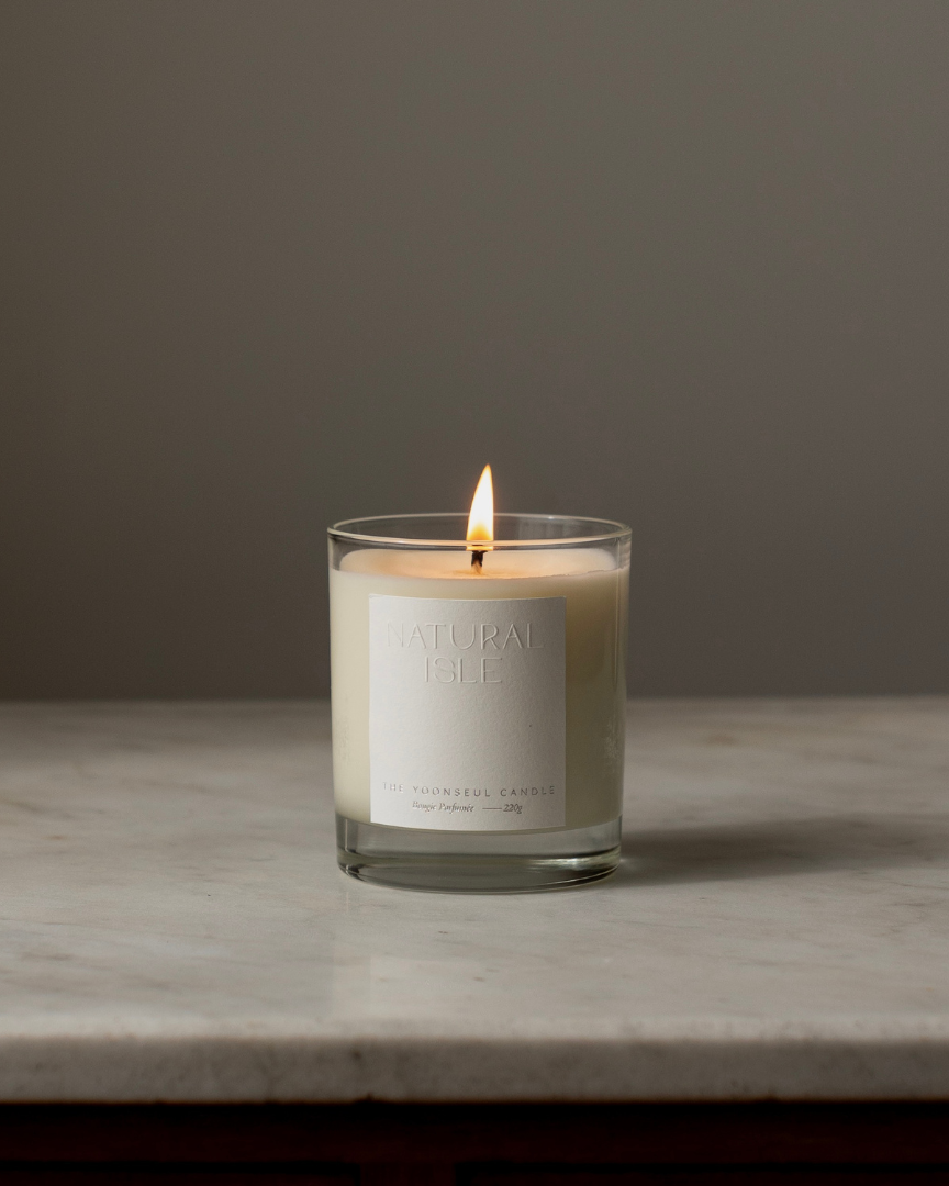 Natural Isle Candle in a glass jar with a label on a marble surface and gray background
