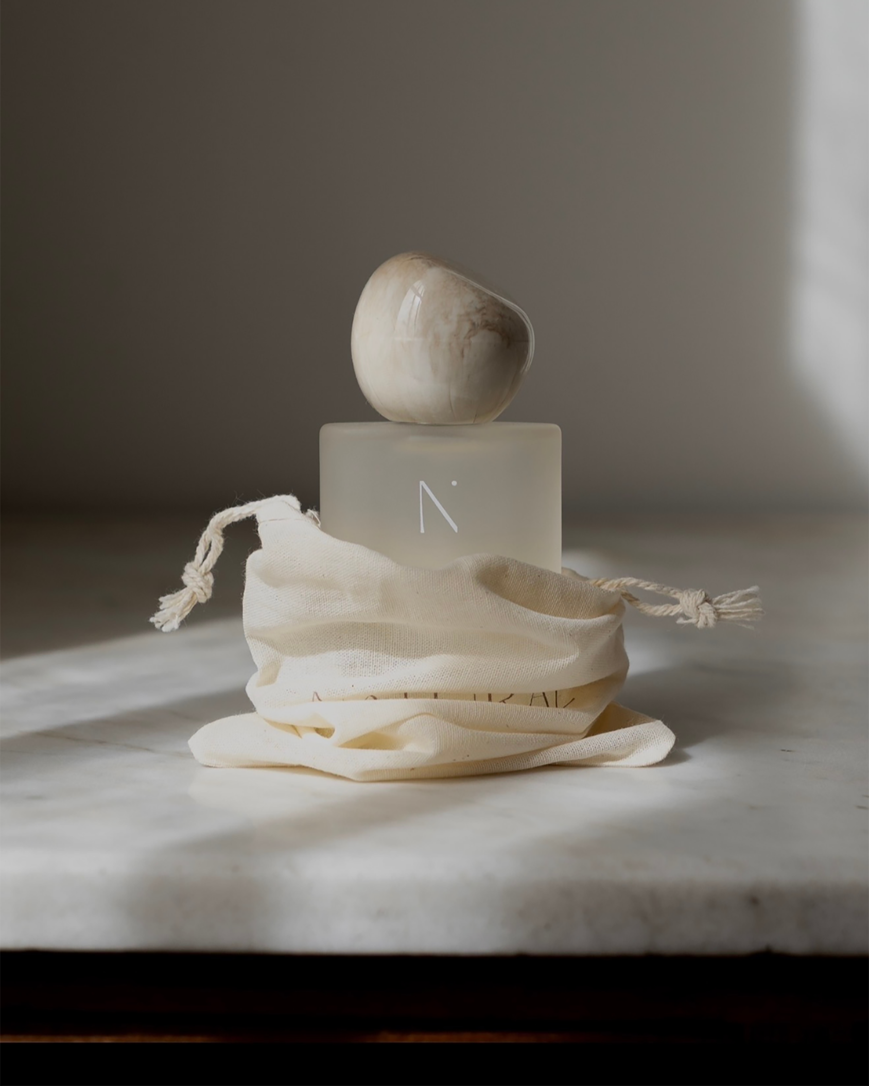 Natural Isle Signature Room Spray, Decorative bottle with a textured canvas bag on a marble surface