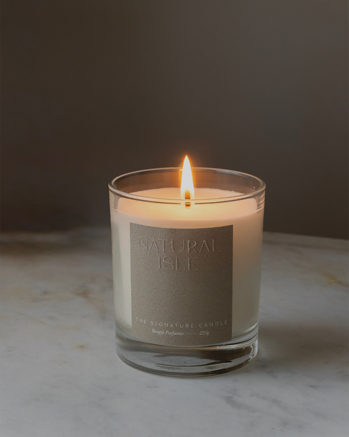 Natural Isle Signature Candle, Lit up Candle with a label on a marble surface