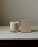 Natural Isle Signature Candle, Glass candle with a beige label on a marble surface next to its packaging box.