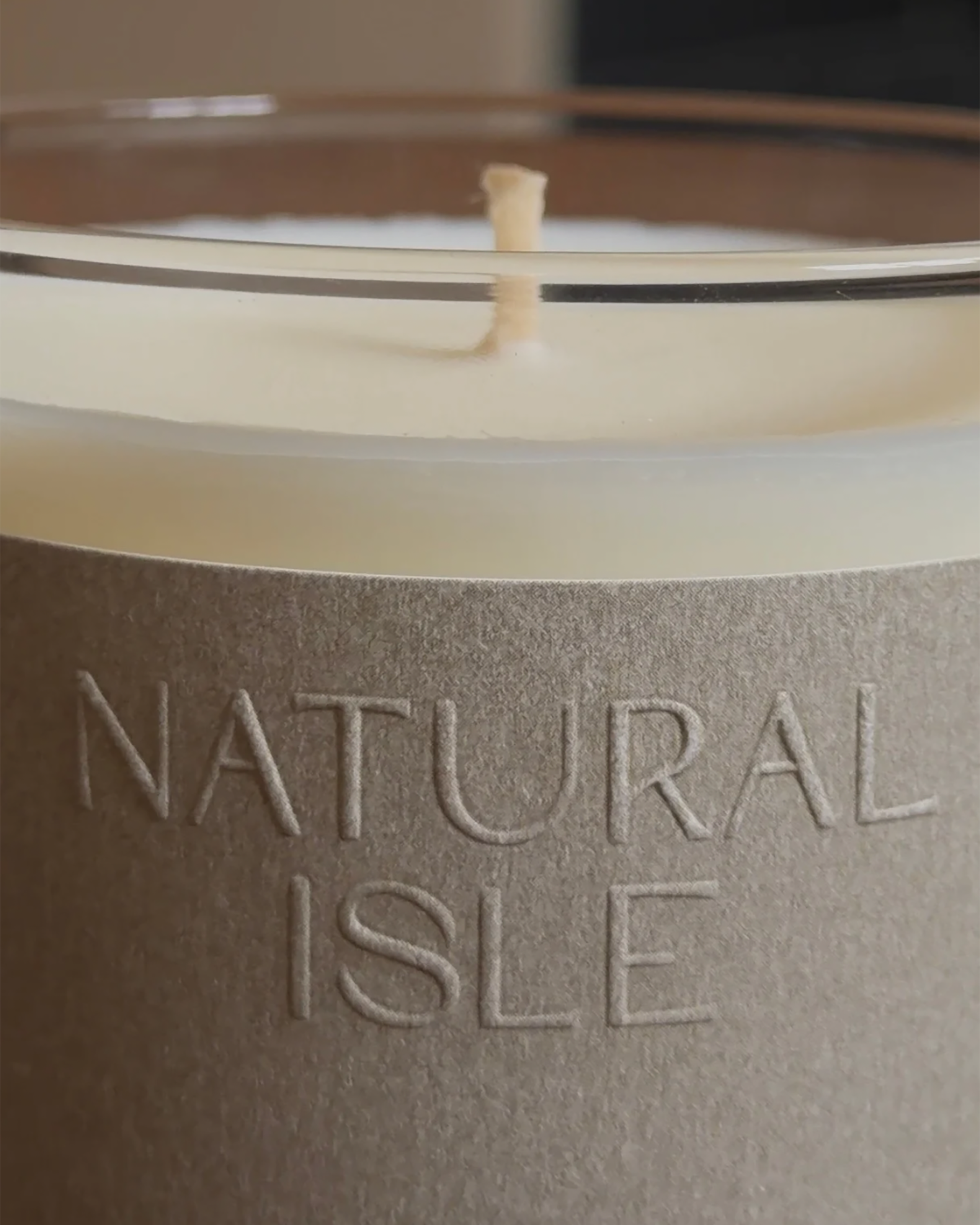 Natural Isle Signature Candle, Close-up of a candle with 'Natural Isle' branding on a neutral background